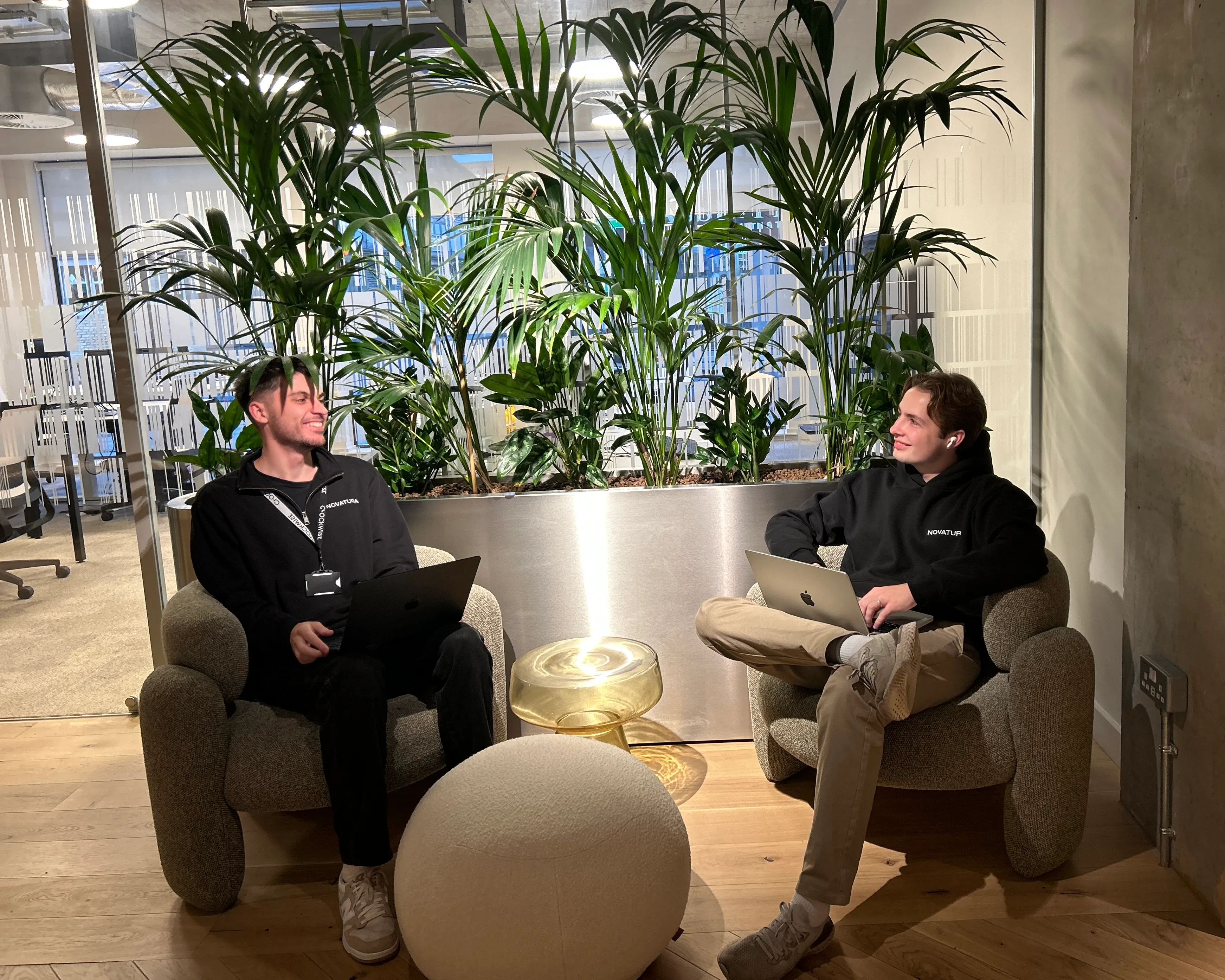 Max and John from Novatura having fun chatting under a plant while sat on comfy chairs